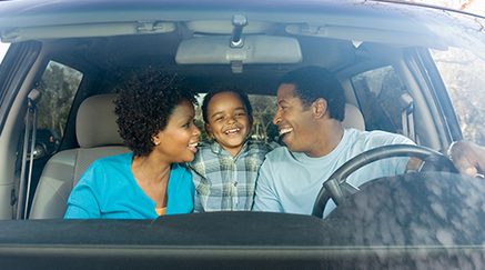 A smiling African American family inside a car.